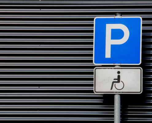 Ein Parkplatzschild für Rollstuhlfahrer vor den Querstreifen einer Jalousienwand.