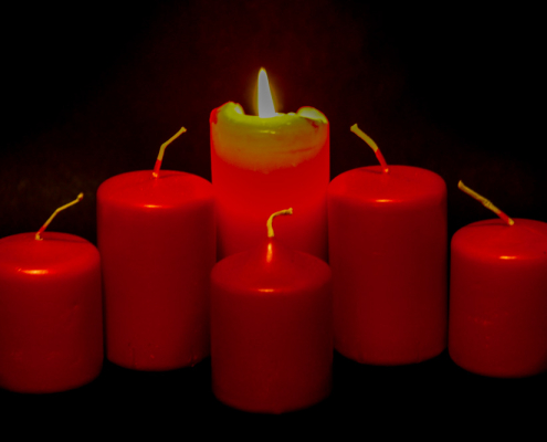 4 rote Kerzen bilden einen leichten Bogen. Von aussen zur Mitte werden die Kerzen immer größer. Die mittlere Kerze brennt als einzige. Vor ihr steht eine 5. kleine Kerze.