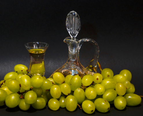 Stillleben mit grünen Weintrauben, die eine Glaskaraffe und ein Glas mit Grappa umgeben