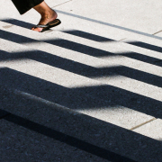 Das Bild zeigt im hinteren Drittel die Füße einer Frau, die mit Flip-Flops eine Treppe hochgeht. Der Vorder- und Mittelgrund wird von Schattenbildern auf der Treppe gebildet.