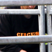Hinter einem vergitterten Tor steht ein Mann, der einen Pullover mit der Aufschrift Circus trägt und an dem Torschloss hantiert.