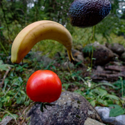 Tomate, Banane und Avokado fliegen in der Luft von einem waldigen und steinigen Hintergrund
