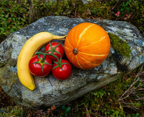 Stillleben von Banane, Tomaten und Kürbis auf einem Stein drapiert