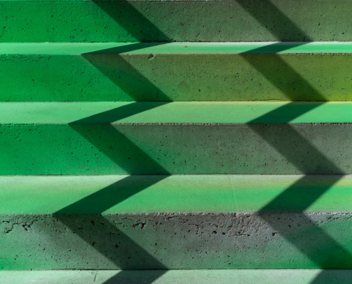 Auf den Stufen einer grünen Treppe bildet der Schatten eines Geländers ein Zickzack.kzack der Schatten