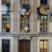 An einem 3stöckigen Haus hängen Menschen kopfüber aus den Fenstern