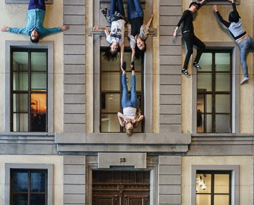 An einem 3stöckigen Haus hängen Menschen kopfüber aus den Fenstern