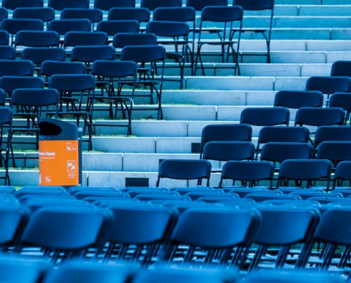 Das Foto zeigt Reihen von blauen Stühlen einer Open Air Veranstaltung. Den Akzent bildet ein Papierkorb mit einem orangefarbenen Aufkleber der BSR.