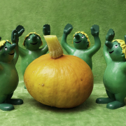 5 grüne Plastikmännchen mit gelben Hut stehen mit erhobenen Armen um einen Kürbis