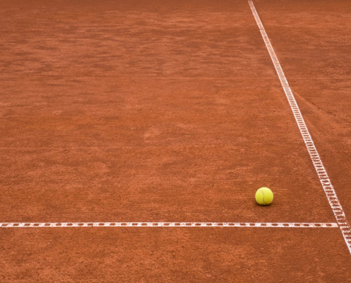 In der Ecke der Feldmarkierung eines Tennisplatzes liegt ein gelber Tennisball.