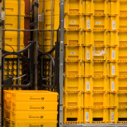 Ein Hochkantfoto, auf dem mehrer Stapel gelber Boxen der Deutschen Post auf einem Rollwagen zu sehen sind.