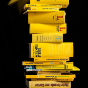 Das hichformatige Foto zeigt einen Bücherstapel, der aus gelben Büchern gebildet wird.