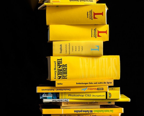 Das hichformatige Foto zeigt einen Bücherstapel, der aus gelben Büchern gebildet wird.