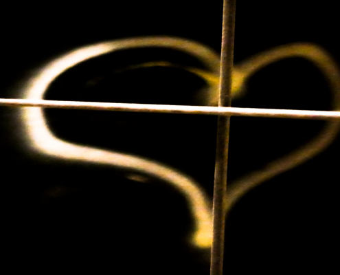 Das querformatige Foto zeigt ein auf schwarzem Untergrund gemaltes gelbes Herz, das von einer waagerechten und einer senkrechten Stange geteilt wird.