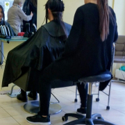 Das hochformatige Foto zeigt eine Situation beim Friseur, bei der einer Frau die langen Haare gekürzt werden.