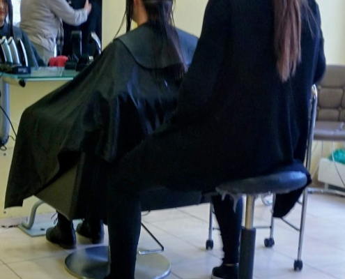 Das hochformatige Foto zeigt eine Situation beim Friseur, bei der einer Frau die langen Haare gekürzt werden.