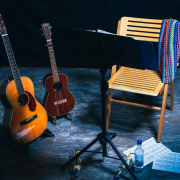 Auf einer Bühne stehen zwei Gitarren im Ständer neben einem leeren Stuhl, der hinter einem Notenständer steht.