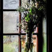 Vor einem Fenster steht in einer Glasvase ein Strauß Wiesenblumen
