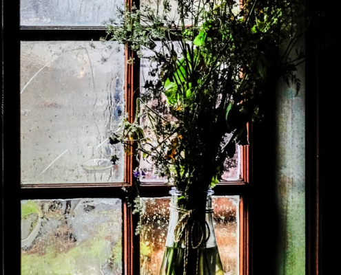 Vor einem Fenster steht in einer Glasvase ein Strauß Wiesenblumen