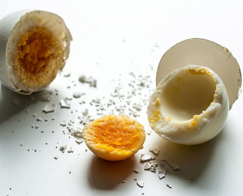 Das querformatige Foto zeigt ein hart gekochtes , in der Mitte geteiltes Ei. Während die linke Eihälfte koplett aus der Schale, dem Eiweiß und dem Eigelb besteht, ist die rechte Hälfte in ihre drei Teile separiert.
