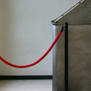 Das hochformatige in grau gehaltene Bild zeigt das Geländer eines Treppenaufgangs aus Stahl. Der Zugang ist mit einer roten Kordel abgesperrt.