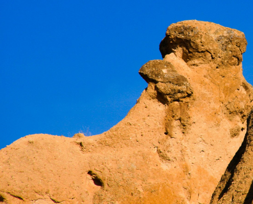 Das querformatige Foto zeigt einen gelb-braunen Felsen, der wie ein Rabengesicht geformt ist.