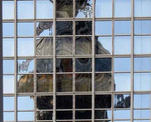 Auf dem hochformatigen Foto sieht man das verzerrteSpiegelbild des Fernsehturms in einer Scheibe.