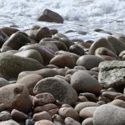 Das querformatige Foto zeigt im Vordergrung graue Steine, die das Ufer eines Meeresküste bilden
