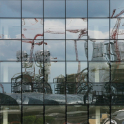 Das querformatige Foto zeigt eine Scheibe, die aus vielen quadratischen Scheiben besteht.In dieser Scheibe erscheint das verzerrte Spiegelbild der Baustelle des Hauptbahnhofs.