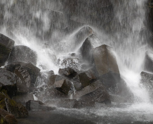 Das querformatige Foto zeigt wie das Wasser einen Wasserfalls auf schwarze Granitblöcke prasselt.