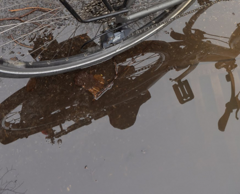 Auf dem querformatigen Foto sieht man das Hinterrad eines Fahrrades, das sich in einer Pfütze spiegelt.