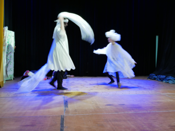 Zwei Kinder tanzen in Weissen Gewändern auf einer Theaterbühne