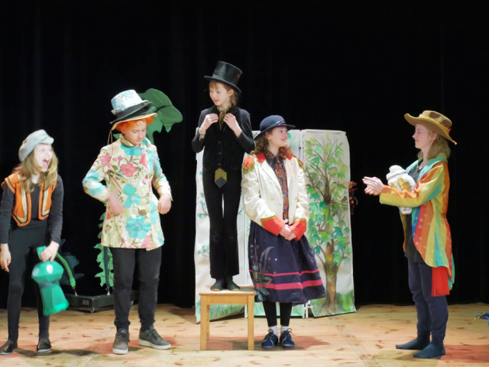 Fünf Kinder in Bunten Kostümen auf einer Theaterbühne, eine steht auf einem Hocker