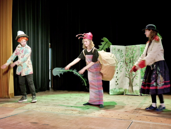 Drei Kinder auf einer Theaterbühne tanzen, eine trägt ein Schneckenkostüm