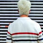 Auf dem querformatigen Foto steht ein Mann in einen quergestreiften Polohemd vor einer Wand mit Querstreifen