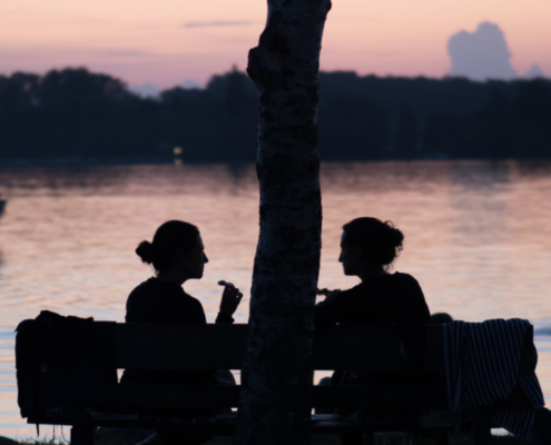 Auf dem hochformatigen Foto unterhalten sich 2 Frauen im Sonnenuntergang und Gegenlicht