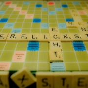 Das querformatige Bild zeigt den Ausschnitt eines Scrabble Spiels, auf dem das Wort 'Verflickst' im Blickpunkt steht. Ein schräg stehender Baustein mit einem X deutet auf den Schreibfehler hin.