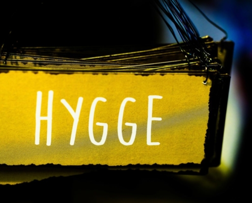 Das querformatige Bild zeigt ein gelbes Schild in dunkelblauer Umgebung, auf dem das Wort 'Hygge' steht.