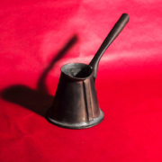 Das querformatige Foto zeigt ein einen kleine Kanne mit langem Stil auf rotem Hintergrund und den Schatten der Kanne.