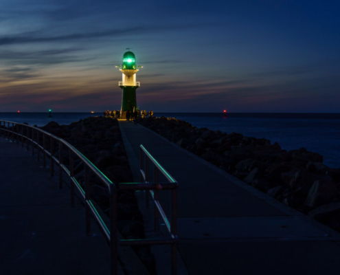 Das querformatige Foto zeit einen Blick auf einen Leuchtturm im Abendlicht.