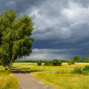 Das querformatige Foto zeigt dunkle Wolken über dem Mauerweg und der grünen Landschaft.