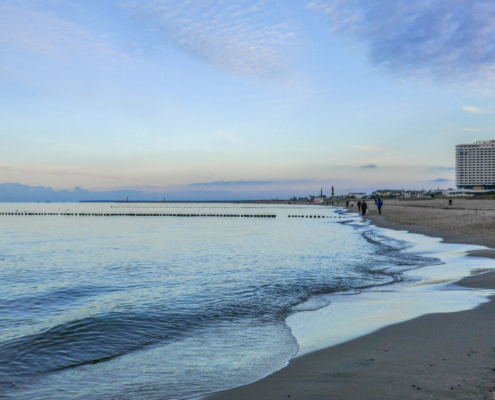 Das querformatige Foto zeigt den Strand der Ostsee bei Warnemünde mit einem Hotelhochhaus.