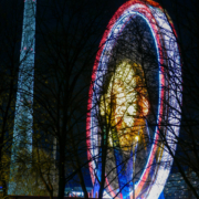 Das hochformatige Foto zeigt ein Riesenrad neben dem Fernsehturm bei Nacht.