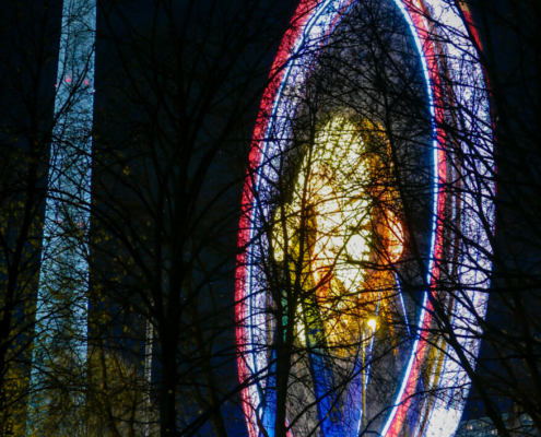 Das hochformatige Foto zeigt ein Riesenrad neben dem Fernsehturm bei Nacht.