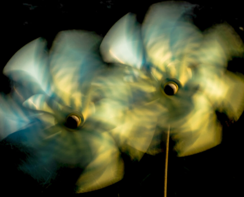 Auf dem querformatigen Foto drehen sich vor schwarzem Hintergrund 2 weiss-blaue Spielzeug-Windmühlen