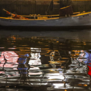 Auf dem querformatigen Foto liegt im oberen Drittel des Bildes ein Ruderboot. Das Boot und die bunte Umgebung über dem Boot spiegeln sich im Wasser.