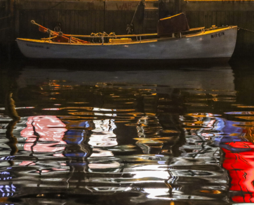 Auf dem querformatigen Foto liegt im oberen Drittel des Bildes ein Ruderboot. Das Boot und die bunte Umgebung über dem Boot spiegeln sich im Wasser.