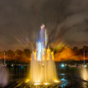 Das querformatige Foto zeigt einen farbig illuminierten Springbrunnen bei Nacht.