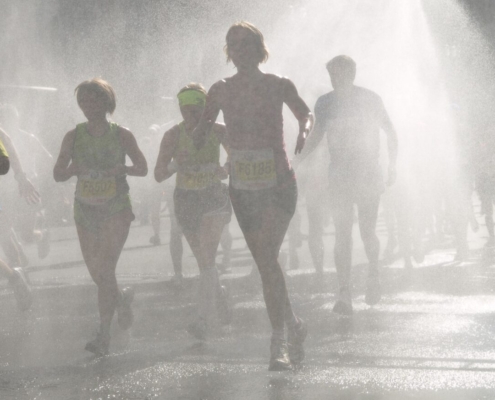 Das querformatige Foto zeigt Marathonläuferinnen und Läufer durch einen Wassersprühnebel.