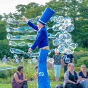 Das hochformatige Foto zeigt einen Stelzenmann, der übergroße Seifenblasen produziert.