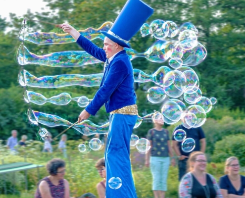 Das hochformatige Foto zeigt einen Stelzenmann, der übergroße Seifenblasen produziert.